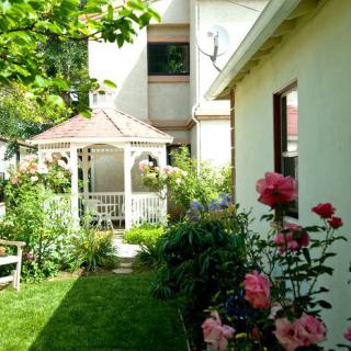 A tranquil garden featuring a white gazebo surrounded by lush greenery and blooming roses.
