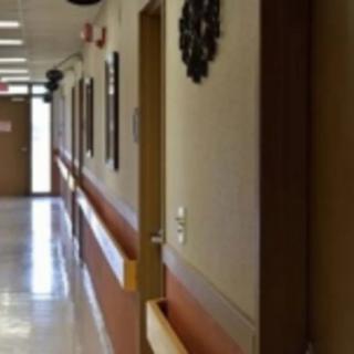 A quiet hospital hallway with open doors and overhead lighting.