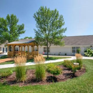 A serene garden with a gazebo and well-maintained landscaping in front of a building on a sunny day.