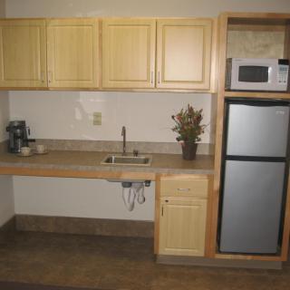 A compact kitchenette with wooden cabinets, a sink, refrigerator, and microwave.