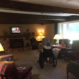 A cozy living room with people watching television, featuring a large window and comfortable seating.