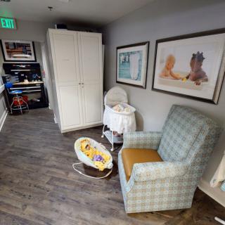 A cozy nursery corner featuring a rocking chair, baby bassinet, and playful artwork.