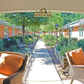 A sunny outdoor seating area overlooking a garden pathway surrounded by trees and shrubs.