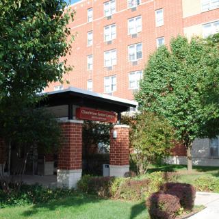 A brick building with a landscaped entrance and surrounding trees.
