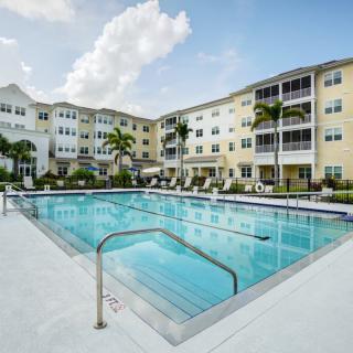 A modern apartment complex with a large outdoor swimming pool surrounded by palm trees.