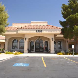 A building with a tiled roof and large entrance located near a parking lot with clear blue skies.