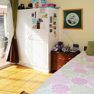A cozy bedroom with sunlight streaming in, featuring a wardrobe adorned with photos and a neatly made bed.