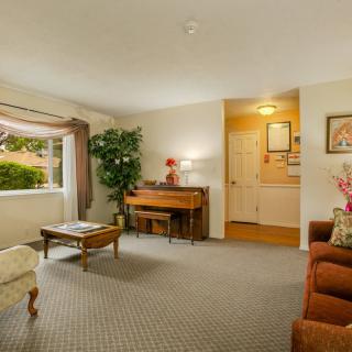 A cozy living room featuring a piano, comfortable seating, and natural light from a large window.