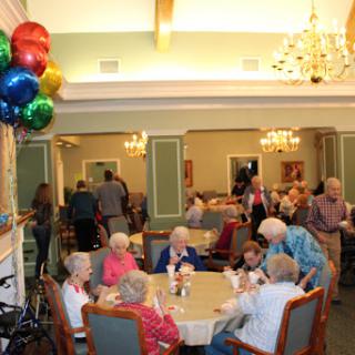 Seniors enjoying a lively gathering in a community dining room adorned with colorful balloons.