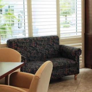 A cozy living room corner with a patterned sofa, chairs, and a table near large windows with blinds.