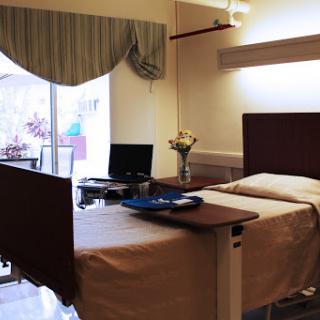 A well-lit hospital patient room featuring a bed, desk, and window.