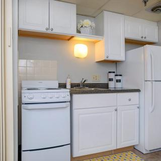 A compact apartment kitchen with white cabinets, a stove, refrigerator, and sink.