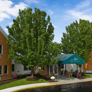 A building entrance with a green awning, surrounded by lush trees and landscaping.