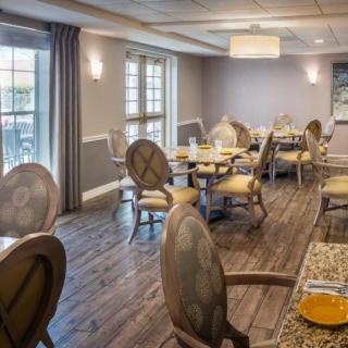 A cozy and elegantly furnished dining area with tables and chairs, complemented by natural light from large windows.