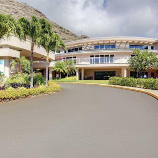 A modern building surrounded by palm trees and landscaped gardens under a partly cloudy sky.