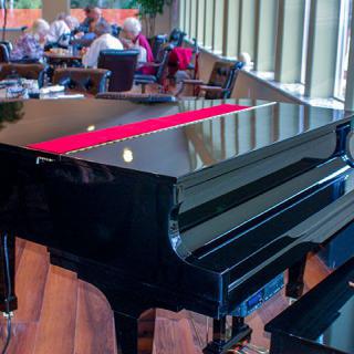 A grand piano in a restaurant setting with diners in the background.