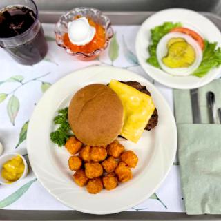 A meal served on a tray featuring a burger, sweet potato tots, salad, and a dessert.