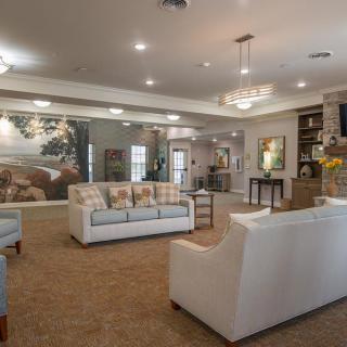 A spacious and elegantly decorated lounge area featuring white sofas, chandeliers, and artwork on the walls.