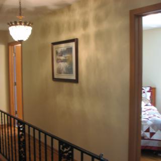 A hallway in a home with a light fixture, painting on the wall, and an open bedroom door.