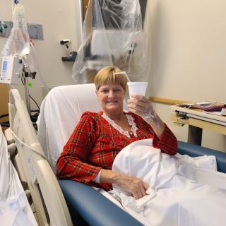 A smiling patient holding a cup while resting in a hospital bed.