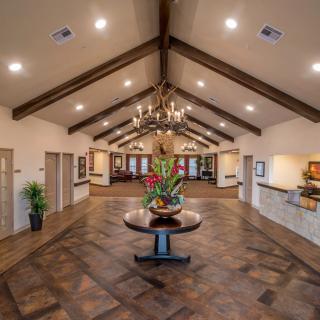 A spacious lobby area with a central table featuring a flower arrangement, illuminated by a chandelier hanging from a vaulted ceiling.