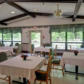 A dining room with neatly arranged tables and chairs, covered in white tablecloths, overlooking a scenic view through large windows.