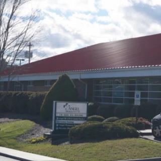 A commercial building with a red roof and a sign in front, set against a partly cloudy sky.