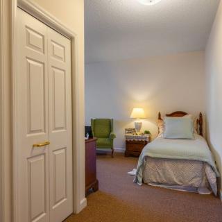 A cozy bedroom with a single bed, a lamp, and a chair in the corner.