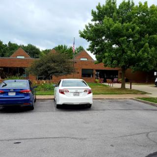 A view of a parking lot with two cars parked in front of a building surrounded by greenery.