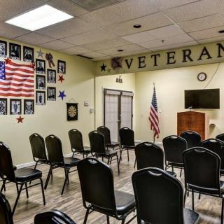 A veterans meeting room with arranged chairs, American flag, and portraits on the wall.