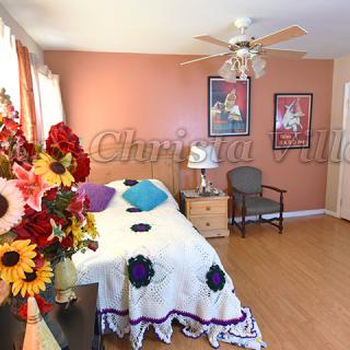 A cozy bedroom with colorful decor and floral accents, featuring a bed, wall art, and wooden flooring.