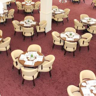An elegantly arranged dining area with round tables and comfortable chairs on a red carpet.