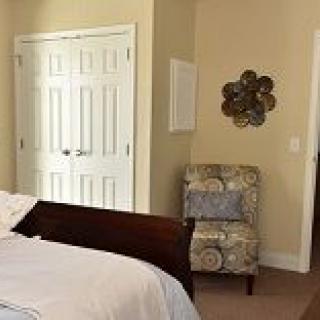 A cozy bedroom featuring a bed, floral-patterned chair, and a closet with double doors.