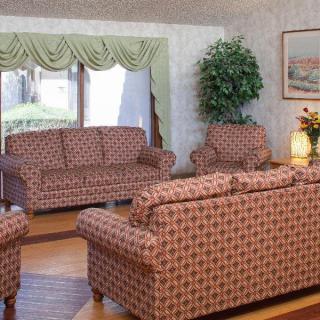 A cozy living room featuring patterned furniture and a large window with green curtains.