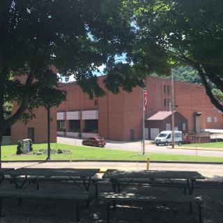 A view of a brick building surrounded by greenery and picnic tables in a park.