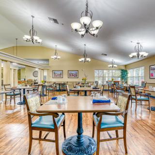 A spacious and well-lit dining area with neatly arranged tables and chairs on a wooden floor.