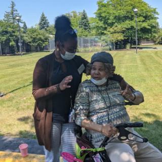 A caregiver and an elderly person enjoying a sunny day in the park.