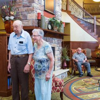 An elderly couple holds hands in a cozy retirement home's living area.