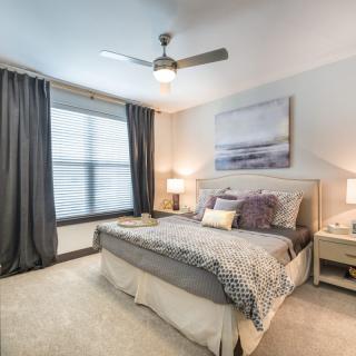 A modern bedroom with stylish decor, featuring a bed, nightstands, and a ceiling fan.