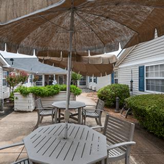 A cozy outdoor patio area featuring tables with umbrellas, surrounded by lush greenery.