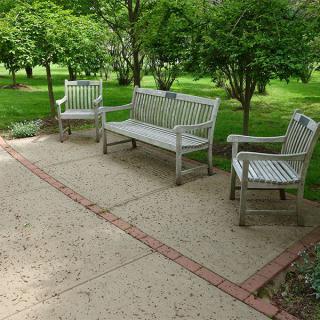 A peaceful garden setting with a bench and chairs on a patio.