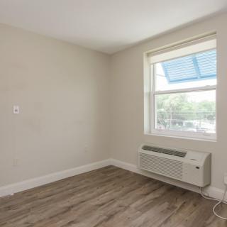 A small empty room with hardwood floors, a window, and an air conditioning unit.