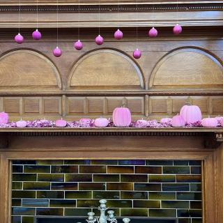 A wooden fireplace mantel decorated with pink pumpkins and hanging ornaments.