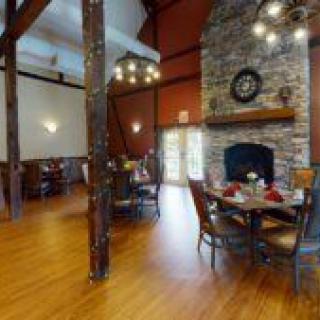 A cozy restaurant interior with a stone fireplace, elegant chandeliers, and wooden flooring.