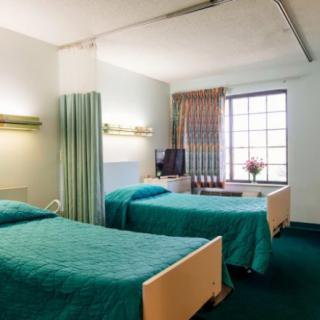 A hospital room with two beds, a television, and a window.