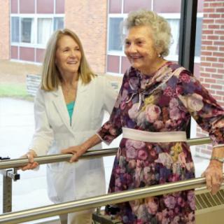 An elderly woman receiving assistance from a healthcare professional during physical therapy.