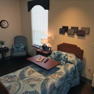 A cozy single bedroom with a decorative bedspread, featuring a bedside table and lamp, accented by wall art and a comfortable chair.