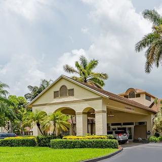 A tropical-style house with palm trees and a landscaped driveway under a cloudy sky.