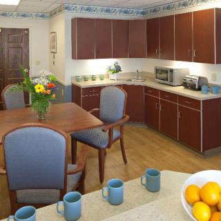 A cozy kitchen and dining area featuring wooden cabinets, a dining table with blue chairs, and a bowl of oranges on the counter.