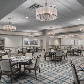 An elegantly decorated dining room with neatly arranged tables and chairs, featuring stylish chandeliers and a patterned carpet.